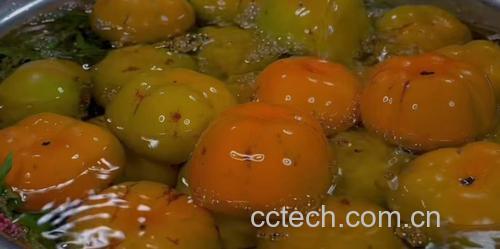 一个透明玻璃盆中盛有约40度温水,几颗青红色的柿子完全浸没在水中,水面微微冒热气,旁边放着一支食品温度计显示40摄氏度,背景为木质厨房台面 温水浸泡脆柿过程图示
