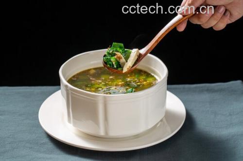一口白色陶瓷汤锅置于燃气灶上,锅中汤水微沸,可见翠绿的荷兰豆段与白色豆腐块翻滚其中,锅边放有生姜片和葱段,蒸汽袅袅升起,背景为整洁现代厨房环境 荷兰豆煮汤过程