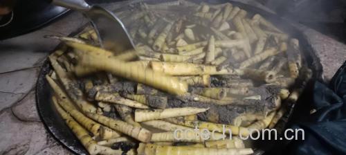 一口不锈钢锅中正在煮着切好的竹笋块,水面微沸,可见少量灰白色浮沫,旁边放着漏勺和姜片,背景为厨房操作台 竹笋焯水过程图