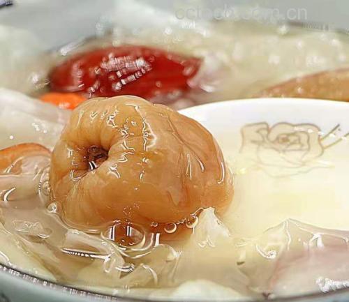 一碗热气腾腾的桂圆肉与西洋参炖水,旁边摆放着新鲜的桂圆果和切片西洋参 桂圆肉与西洋参炖水