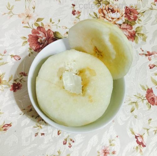 一碗热气腾腾的冰糖炖香梨摆放在木质餐桌上,梨子完整呈半透明状,内部可见融化的冰糖光泽,周围点缀着红色枸杞,背景为温暖灯光下的厨房环境 冰糖炖香梨成品展示