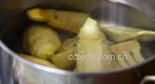 新鲜竹笋被放入沸水中焯烫,锅中有蒸汽升腾,旁边摆放着未处理的竹笋段和已焯好的淡黄色竹笋片,背景为厨房操作台 竹笋焯水过程示意图
