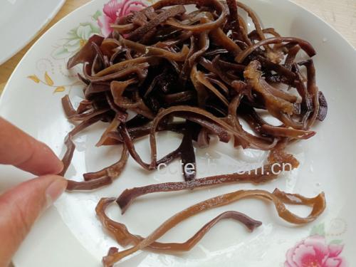 一位家庭主妇正在厨房操作台上处理泡发好的黑木耳,手握剪刀修剪根部,旁边碗中是已泡发的黄豆,灶台上砂锅正冒着热气,锅盖半开,蒸汽升腾,环境整洁温馨 家庭厨房炖煮过程场景
