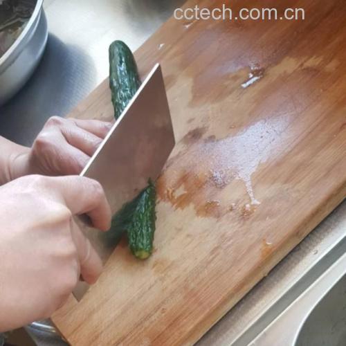 一名厨师正在操作台上用清水冲洗新鲜的小黄瓜,旁边摆放着干净的砧板和刀具,几根已切半的小黄瓜整齐排列,背景为明亮厨房环境 小黄瓜清洗与切割过程