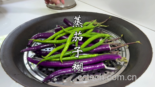 一位中年女性在家中厨房操作台上准备蒸茄子,将切好的整根紫长茄放入竹制蒸笼中,旁边放有蒜瓣和香菜,背景可见燃气灶与计时器,营造出健康家常烹饪氛围 家庭蒸茄子制作过程