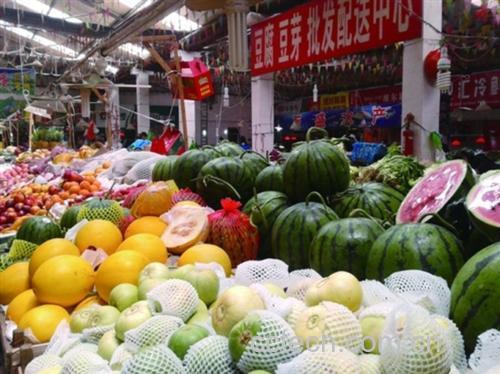 农贸市场摊位上陈列多种甜瓜和桃子,包括网纹哈密瓜、绿皮羊角蜜、黄桃和水蜜桃,摊主正在向顾客介绍果实特点,背景有价格牌和‘新鲜采摘’标识,体现真实消费场景 水果市场选购场景