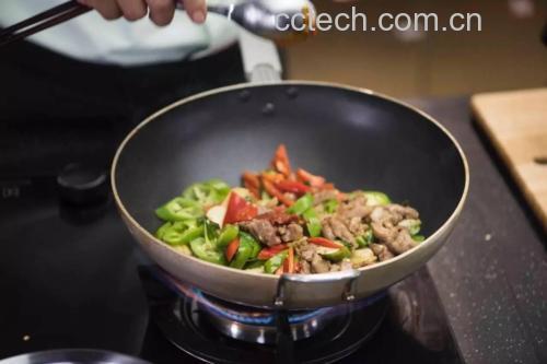 一名穿着围裙的女性正在燃气灶前翻炒锅中的牛肉与萝卜,锅中食材翻滚,散发蒸汽,展示牛肉炒萝卜的实际烹饪过程 一位中年女性在厨房用锅翻炒牛肉与萝卜,动作自然,背景整洁明亮