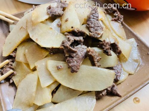 新鲜白萝卜与红色牛肉整齐切片置于木砧板上,周围配有葱段、姜片、大蒜瓣等辅料,展现牛肉炒萝卜的原材料准备场景 白萝卜与新鲜牛肉切片摆放在木质砧板上,旁边有葱姜蒜调料,背景为厨房灶台