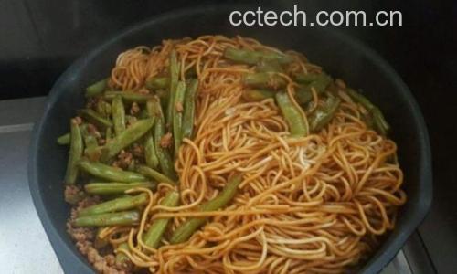 炒锅中正在翻炒的豆角与茄子混合物,色泽油润发亮,蒜末清晰可见,锅气升腾,体现家庭灶台烹饪的真实氛围 豆角和茄子正在炒制过程中的特写镜头