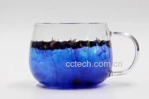 一杯透明玻璃杯中盛放着淡黄色的液体,里面漂浮着几片干韭菜叶和红色枸杞,背景为木质餐桌 韭菜枸杞泡水