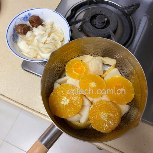 一位家庭主妇正在厨房操作台前准备炖梨,桌上摆放着新鲜雪花梨、红枣、冰糖和玻璃炖盅,炉灶上砂锅正微微冒热气,窗外可见秋日落叶,营造出温馨养生氛围 厨房炖煮场景