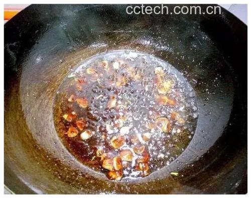 一口黑色铁锅正置于燃气灶上,油面微微波动并泛起细小油纹,厨师手持筷子夹起一段裹好粉的带鱼,准备放入热油中,背景有姜片和调料瓶 热锅热油煎带鱼过程
