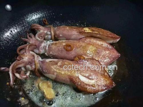 一位厨师正在家庭厨房中用铁锅快速翻炒油菜,旁边放着蒜末和酱油等调料 家庭厨房中正在翻炒油菜的画面