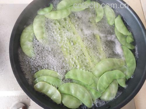 厨师正在灶台前用大铁锅翻炒荷兰豆,火焰升腾,锅中蔬菜呈鲜绿色,动作熟练,展现高温快炒过程 图片描述