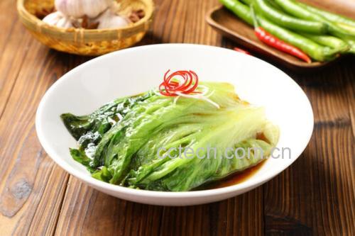 一盘清蒸生菜摆放在白色瓷盘中央,菜叶呈半透明翠绿色,整齐呈放射状排列,表面淋有光泽的棕色酱汁,点缀着金黄的炸蒜粒和红色细椒丝,背景为浅灰色厨房台面,光线柔和 清蒸生菜特写