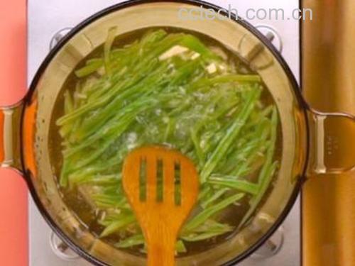 一名厨师正在使用中式铁锅快速翻炒豌豆角,食材呈翠绿色,锅中有轻微火焰升腾,体现‘旺火快炒’的烹饪场景 厨房操作台上摆放着洗净切段的豌豆角、大蒜、红椒片和橄榄油,旁边是一口正在翻炒的中式炒锅,热气腾腾
