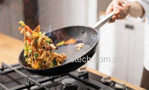 一位厨师正在灶台前翻炒锅中的京葱鸡腿肉,火焰升腾,锅铲翻飞,食材在空中短暂抛起,背景为整洁现代厨房环境 厨房操作场景图