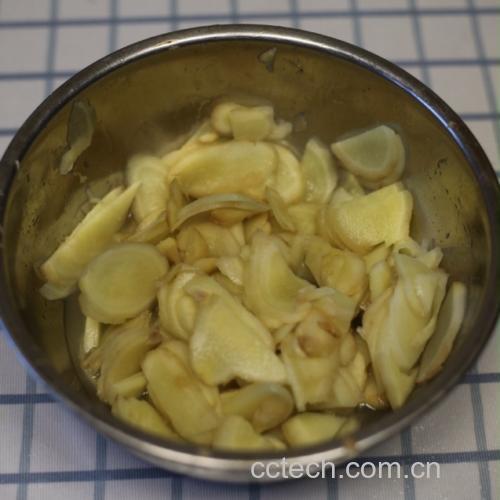 一位厨师正在陶瓷锅中慢火熬煮大黄姜片,锅中水汽升腾,旁边摆放着新鲜姜块、茶杯和木勺,台面上铺有竹制厨具垫,整体氛围温暖舒适 厨房中正在熬制姜茶的场景