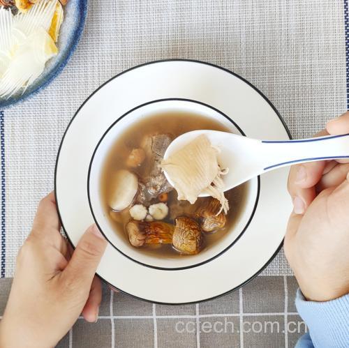 一碗热气腾腾的红参鱼胶煲鸡汤,汤色金黄透亮,表面浮有少量油花,碗中可见完整的鸡块、淡黄色的红参片和半透明的鱼胶,背景为木质餐桌与中式砂锅,营造出温暖养生的氛围 红参鱼胶煲鸡汤的整体成品图