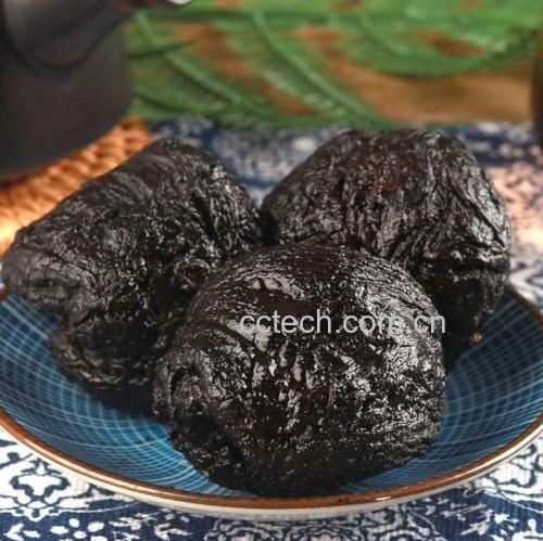 特写镜头展示一双不锈钢镊子正将一条深褐色的乌梅肉小心地插入一个红色圣女果的中心孔洞中,果体完整,周围有几颗已完成的成品,背景为白色陶瓷盘 一只手正用镊子将乌梅条插入挖空的圣女果中