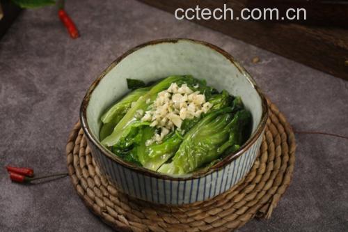 一盘刚出锅的蒜蓉炒散叶生菜特写,叶片翠绿饱满,表面泛着油光,可见细碎的金黄蒜末均匀分布,摆放在白色瓷盘中,背景虚化,突显菜品的色香味诱人 蒜蓉快炒散叶生菜成品图