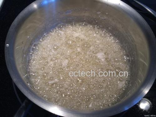 不锈钢奶锅中正在沸腾的深褐色豆浆,蒸汽升腾,锅边可见细腻泡沫,炉火适中,旁边放有 wooden spoon 和量杯 正在煮沸的熟地黄豆浆锅具特写
