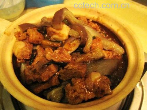砂锅红烧长茄成品特写，深紫黑色茄块完整饱满，表面裹覆琥珀色浓稠酱汁，点缀翠绿葱花与金黄蒜末，砂锅边缘微冒热气，展现低温慢煨形成的柔润质地