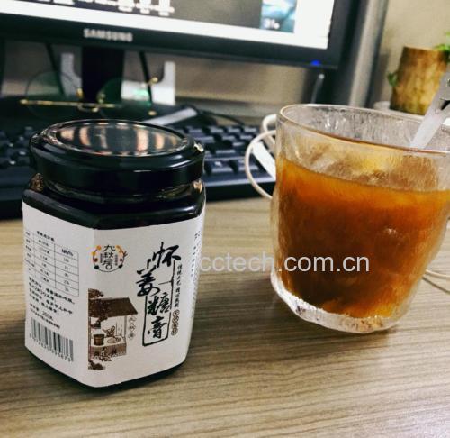 一位女性正在用热水冲调杯中的姜面与红糖混合物,热气升腾,杯子透明可见棕红色液体逐渐溶解,桌面上放有玻璃罐装的姜面和块状红糖,突出家庭养生场景 姜面红糖水冲泡过程