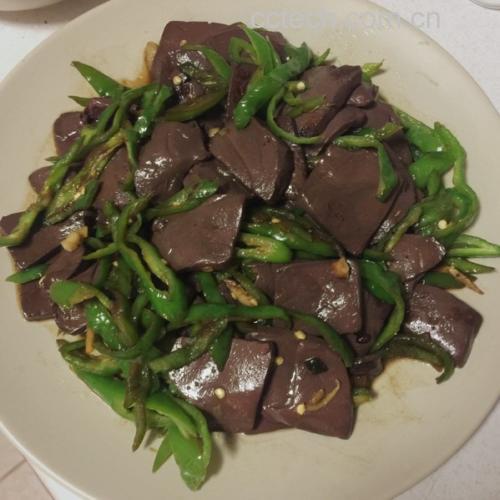 厨师正在用锅铲翻炒锅中的尖椒与猪血混合物,火焰适中,食材呈现金黄色光泽,尖椒翠绿、猪血完整不碎,锅边可见轻微酱汁汽化痕迹 烹饪过程图