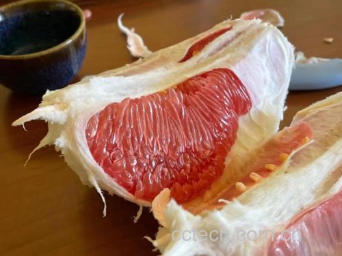 红心柚果肉切成薄片,呈现清晰纹理和饱满汁水,背景为木质桌面,营造自然健康的氛围 红心柚果肉切片展示
