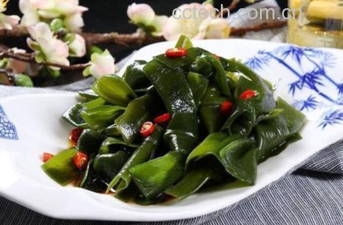 白色瓷碗中浸泡着已泡发的墨绿色海带丝,质地柔韧富有光泽;旁边小锅中正在炖煮海带排骨汤,汤色乳白,配有胡萝卜片和葱段,灶台上有酱油瓶和调料罐,体现家庭烹饪氛围 干海带泡发与烹饪过程