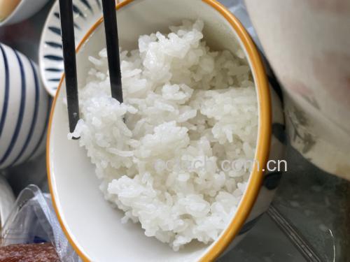 一碗白米饭旁盛着一份香芹炒五花肉,筷子夹起一块肉和几根香芹,画面温馨诱人 香芹炒五花肉配米饭图