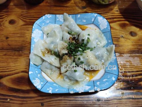 一间明亮的餐厅内,一家三口围坐在木桌旁,桌上摆着一盘热气腾腾的白色饺子,每人面前都有小碟蘸料,孩子正夹起一个饺子开心地笑着,背景墙上挂着中国风装饰画 一家人围坐餐桌享用香芹饺子的温馨场景