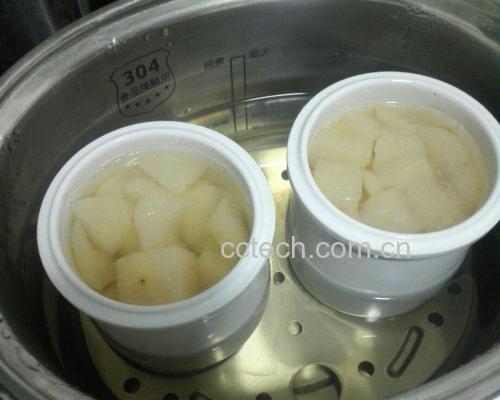 一口不锈钢蒸锅正在冒热气,揭开一角可见内部摆放着一个透明硅胶模具,其中分层清晰可见:白色与淡粉色交替的糯米层之间夹着整齐排列的蜜桃片,顶部光滑完整,色泽温润 蒸制中的蜜桃糯米甜糕