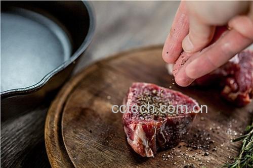 一位厨师手持不锈钢胡椒研磨器,在牛排上方旋转研磨,新鲜黑胡椒颗粒洒落在焦香的肉表面;背景为明火炉灶,光线温暖,突出‘现磨’带来的质感与仪式感 厨房中使用胡椒研磨器现场研磨黑胡椒的场景