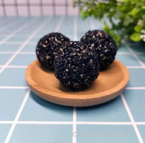 展示几颗手工制作的黑芝麻球,摆放在木质托盘上,背景为厨房环境 黑芝麻球成品展示