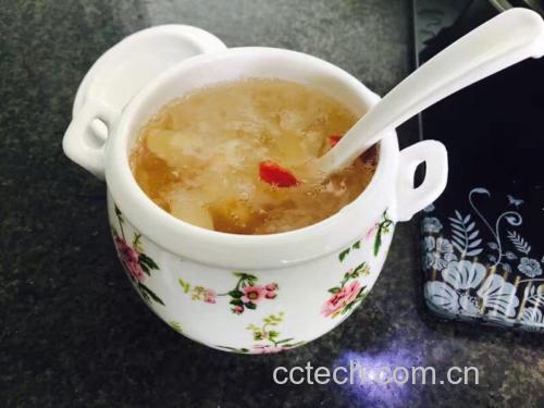 一口白色陶瓷砂锅中正在小火炖煮银耳羹,汤体已呈乳白色微稠状,表面泛着光泽,旁边摆放着冰糖、枸杞和红枣片 炖煮中的银耳羹
