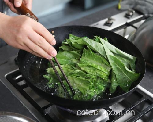 一名家庭主妇正在燃气灶前用铁锅大火翻炒锅中的绿色生菜,锅中热气腾腾,蒜片清晰可见,动作流畅,展现快炒的真实厨房场景 清炒生菜翻炒过程