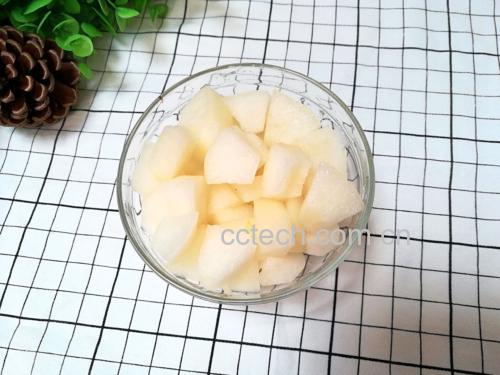一位中年女性正在厨房操作台前处理刺梨果实:戴手套去除外皮刺毛,旁边放置玻璃榨汁机、量杯和装有淡黄色液体的玻璃杯。台面整洁,背景可见冰箱和现代厨具,体现家庭健康饮食场景 女性在厨房准备刺梨饮品