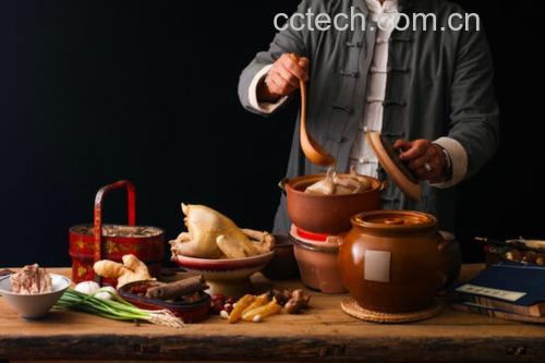 一个中式厨房环境中,一位女性正在用白色陶瓷砂锅炖煮鹿鞭鸡汤,锅中漂浮着鹿鞭片、鸡肉块、枸杞和姜片,热气腾腾,旁边摆放着装有干鹿鞭片的玻璃罐和中药材袋,整体氛围温馨养生 家庭炖煮鹿鞭汤场景