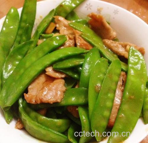 一道刚出锅的猪肉炒荷兰豆盛放在圆形白色瓷盘中央,荷兰豆翠绿鲜亮,肉片分布均匀,表面泛着诱人的光泽,旁边配有半碗白米饭,背景虚化,营造温馨家庭用餐氛围 成品装盘效果图