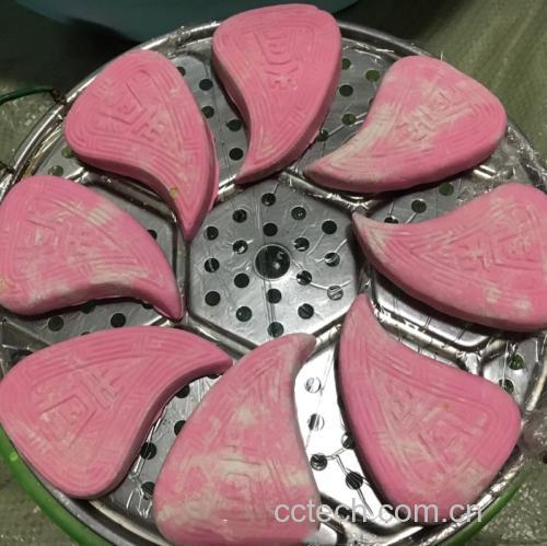 一位潮汕妇女正在操作台前手工包制红桃粿:左手托着面团,右手正在包裹馅料,旁边放置着木制红桃粿模具和已压制完成的桃形生坯 图片描述