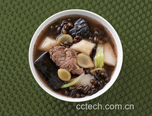 一碗热气腾腾的黑豆炖排骨,汤色浓郁,黑豆软糯,搭配绿色香菜点缀,盛放在白色瓷碗中,背景为厨房木质台面,体现家常健康饮食氛围 黑豆料理场景