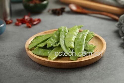 一位厨师正在案板上用手指逐一为荷兰豆掐头去尾,并撕除两侧纤维筋络,旁边放着一碗已处理好的翠绿荷兰豆,背景为厨房操作台,光线明亮自然 荷兰豆清洗与去筋处理过程