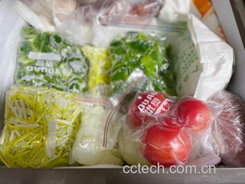 一个透明保鲜盒内竖立放置几株山芹菜,根部浸在浅层清水中,上方覆盖半开的保鲜膜,整体置于冰箱蔬菜格中,旁边无其他水果,展示科学冷藏布局 家庭冰箱中正确储藏山芹菜的方式示意图