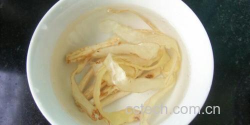 玻璃碗中正在冷水泡发的腐竹,水质清澈,腐竹呈半透明状,展现良好泡发状态,背景有原始干腐竹样本 腐竹在透明玻璃碗中浸泡于清水中,旁边放有未泡发的干腐竹条作为对比