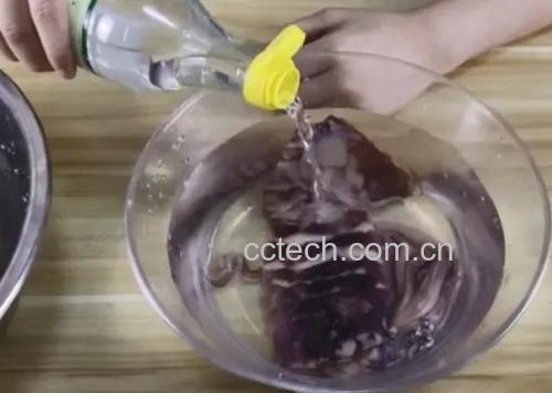 一位主妇在厨房水槽中将切好的白莲藕片放入装有淡黄色液体(醋水)的透明玻璃碗中浸泡,旁边放置柠檬和白醋瓶,展现家庭护色清洗过程 家庭厨房中清洗白莲藕的场景