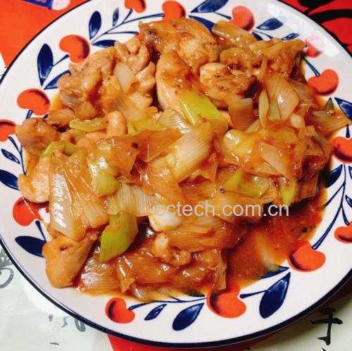 平底炒锅中正在翻炒的大葱鸡腿肉,锅内葱白与鸡块混合,酱汁浓郁,厨师手持锅铲正在颠锅,灶台火焰适中,背景为整洁厨房环境 烹饪过程图