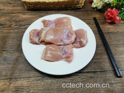 新鲜鸡腿肉被切成均匀小块,旁边摆放着斜切的京葱段,背景为木质砧板与不锈钢刀具,光线自然明亮 食材切配示意图