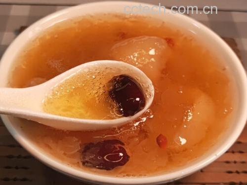 一碗养生粥中加入石硖龙眼干、红枣、莲子、枸杞等食材,色彩丰富,热气腾腾,旁边摆放几颗完整的新鲜石硖龙眼和干燥龙眼肉,展示其多种食用方式 石硖龙眼入膳搭配图